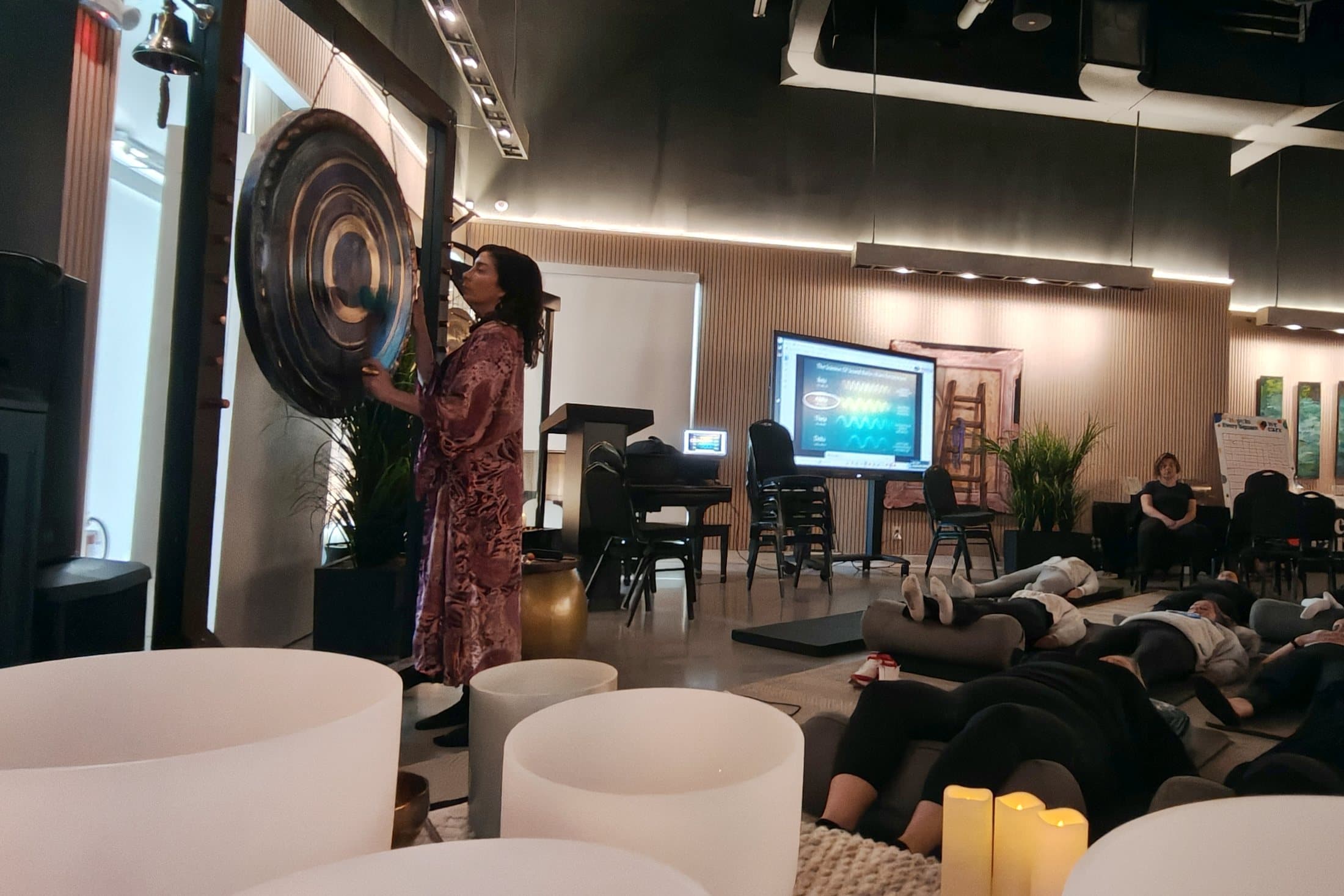 Jennifer Spencer playing a large gong to a room of people lying down