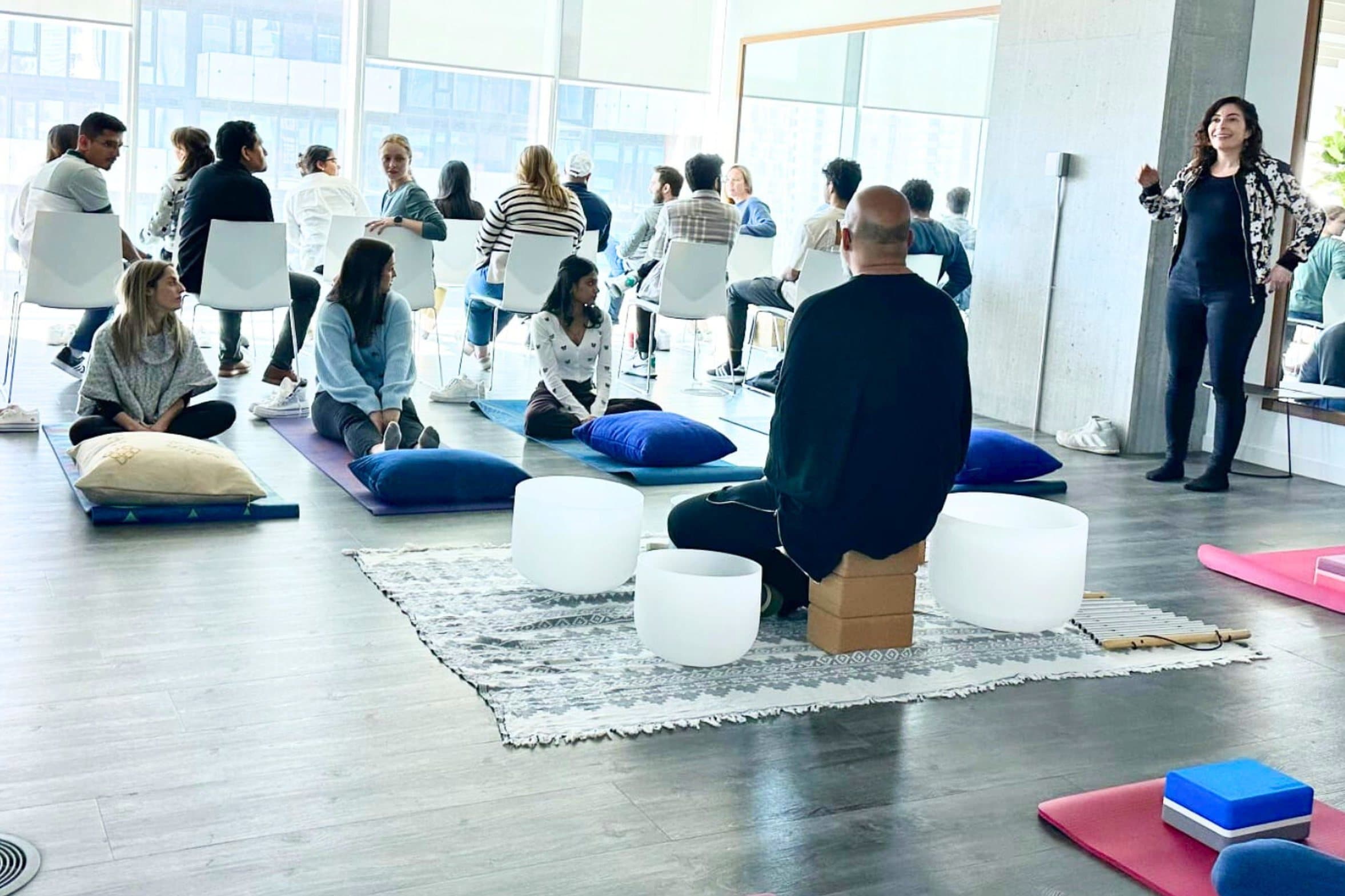 Jennifer Spencer leading a session in a corporate room, with Steve Fernandez at the singing bowls